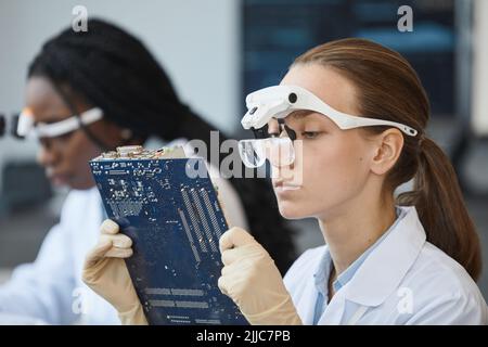 Side view portrait of young female engineer inspecting computer parts at quality control line Stock Photo