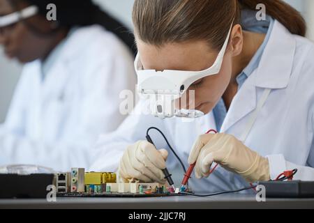 Close up portrait of young female engineer inspecting computer parts with magnifiers at quality control line Stock Photo