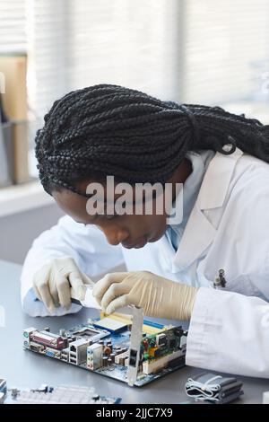 Vertical portrait of black female engineer working with electronic parts in laboratory Stock Photo