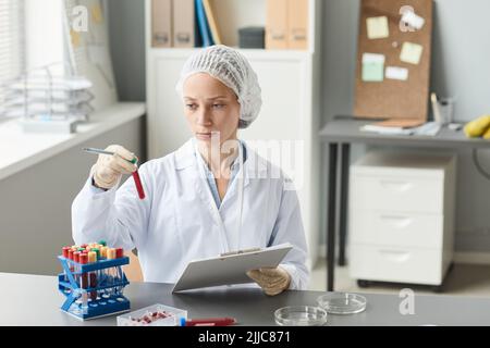 Portrait of female lab technician mixing liquid in test tube while working with blood analysis in laboratory, copy space Stock Photo