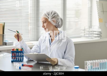 Side view portrait of young medical technician holding test tubes with blood samples in laboratory, copy space Stock Photo