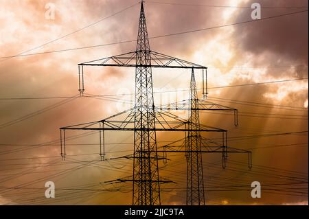 Many elecrtic poles in front of sky with clouds Stock Photo