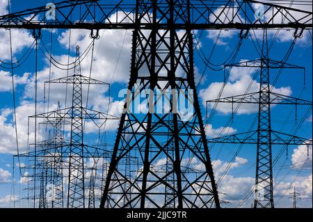 Many elecrtic poles in front of sky with clouds Stock Photo