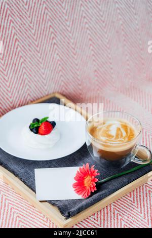Cup of coffee, Pavlova dessert cake, gerbera flower and blank postcard with copy space on the tray with gray napkin. Breakfast for loved one. Romantic Stock Photo
