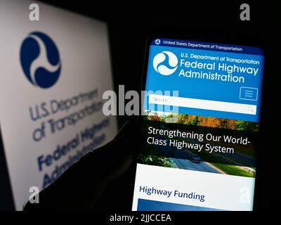 Person holding cellphone with website of US Federal Highway Administration (FHWA) on screen in front of logo. Focus on center of phone display. Stock Photo