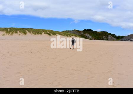 Man with a stick walking on sand, Broadhaven south beach, Stackpole, Pembrokeshire, Wales Stock Photo