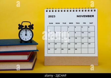 November 2023 desk calendar with books and alarm clock on yellow background. Calendar concept Stock Photo
