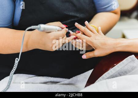Manicurist is applying electric nail file drill to manicure on female fingers. Stock Photo