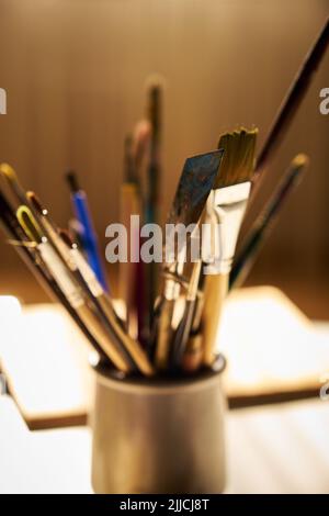 in the beautiful lighting on the table in a glass there are different paint brushes Stock Photo
