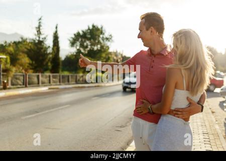 Happy young couple hitchhiking on the road. Traveling, transport concept. Stock Photo