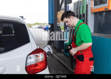 A Down syndrome man employee fueling car at gas station. Stock Photo