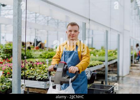 A young employee with Down syndrome working in garden centre, using hand pallet stacker. Stock Photo