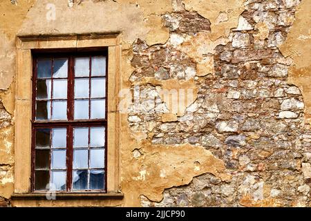 Window with frame from which the paint is peeling off, in a wall of hewn natural stone from which the plaster is falling off Stock Photo