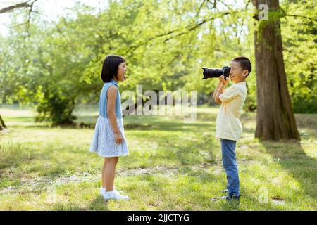 Cute little asian boy acting like a professional photographer while taking photos of his little sister Stock Photo