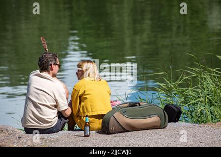 Couple sitting on the bank Lapinlahti Bay on a summer day in Helsinki, FInland Stock Photo