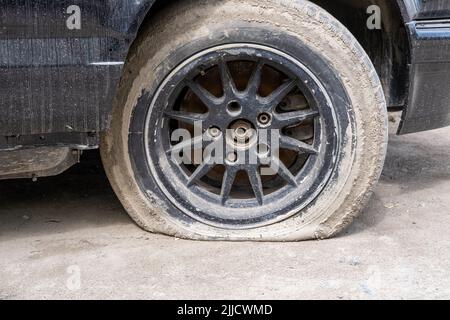 Close-up Of A Damaged Flat Tire Of A Car On The Road. Old wheel car dirty and flat tires. Punctured wheel of a modern car on the road. Car tire punctu Stock Photo