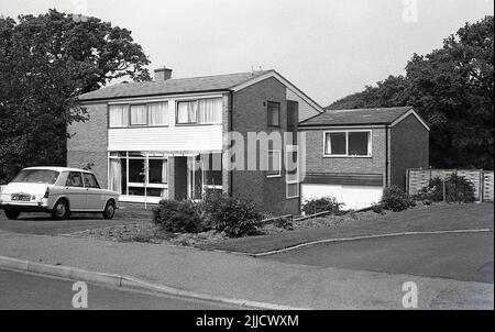 1970s, historical, exterior, front view of a modern house of the era, a common architectural design see on many new housing estates in Britain, from the late 1960s, through the 1970s. Functional and relatvely quick to build, they had large pre-made window panels, which on the plus side meant lots of light and larger - and more - rooms than previous homes. A popular car of the era, an Austin ( or Morris) 1100 car is parked on the driveway. Stock Photo