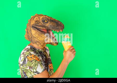Man wearing dinosaur animal head mask drinking cocktail or fruits juice isolated on green background. Stock Photo