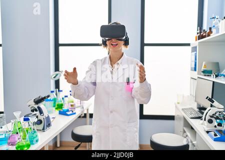 Young woman wearing scientist uniform using virtual reality goggles at laboratory Stock Photo