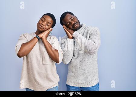 Young african american couple standing over blue background together sleeping tired dreaming and posing with hands together while smiling with closed Stock Photo