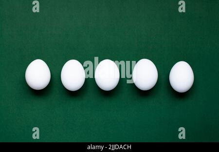 Five white eggs lie on a dark green background Stock Photo