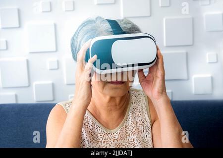 VR glasses using by Asian senior female, the grandma. Retired woman holding VR goggles in her hands and exciting while watching via glasses. Reality v Stock Photo