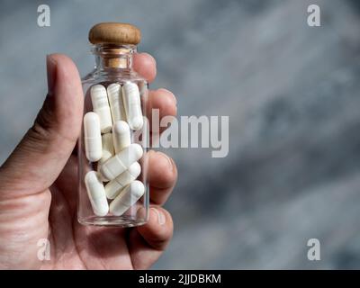 Close up white vitamins or supplements in the small clear glass bottle vials in person's hand with copy space. Hand holding vials with drug capsules. Stock Photo