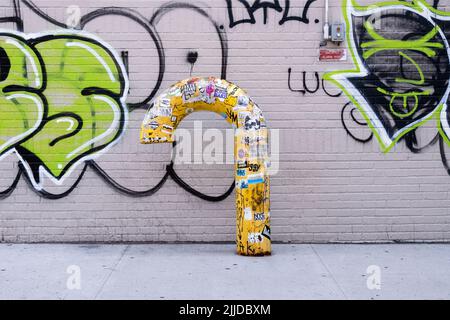 URBAN LANDSCAPE. A yellow candy cone shaped pipe against a graffiti filled wall. On Second Avenue in Greenwich Village. wall. Stock Photo