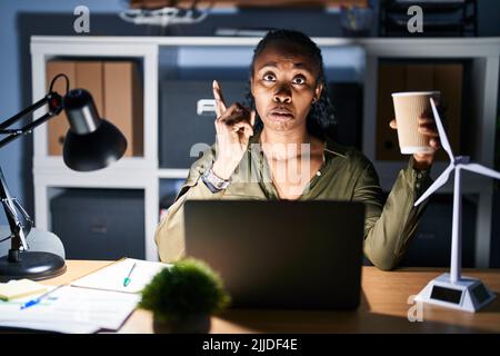 African woman working using computer laptop at night pointing up looking sad and upset, indicating direction with fingers, unhappy and depressed. Stock Photo
