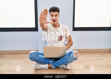 Young hispanic man using laptop at home doing stop gesture with hands palms, angry and frustration expression Stock Photo