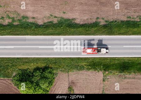 Agricultural tractor with crop sprayer attached driving along the road through countryside landscape, drone pov directly above aerial shot in agricult Stock Photo