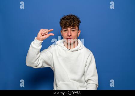 Unhappy young man looking disappointed and showing a small gesture, a small amount or a downscale sign, a few centimeters. Indoor studio shot isolated Stock Photo