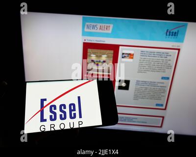Person holding smartphone with logo of Indian media company Essel Group on screen in front of website. Focus on phone display. Stock Photo