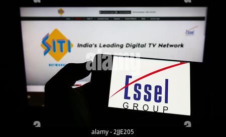 Person holding cellphone with business logo of Indian media company Essel Group on screen in front of webpage. Focus on phone display. Stock Photo