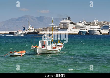 Mykonos, Greece - June 2022: small fishing boat mooored in the harbour with luxury motor yachts and a cruise ship in the background Stock Photo