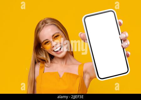 Joyful young woman in colorful sunglasses holding smartphone, mockup Stock Photo