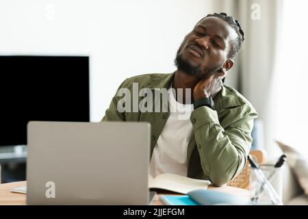 Neck ache. Upset african american guy massaging aching neck, suffering from pain after computer work, sitting workplace Stock Photo