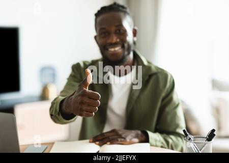 Happy african american man sitting at desk and showing thumbs up sign gesture while working or studying remotely Stock Photo
