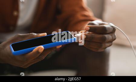 Unrecognizable african american male hands plugging a charger in modern smartphone, closeup, cropped Stock Photo