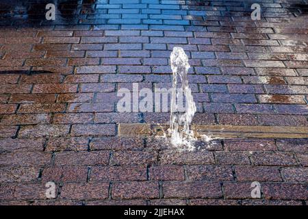 water fountain from a street of red cobblestones in sunlight Stock Photo
