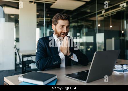 Excited businessman celebrating great news and luck, looking at laptop screen in joy, sitting in office interior Stock Photo