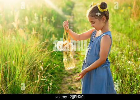 Cute little girl holding a knitted bag with a bouquet of daisies Stock Photo