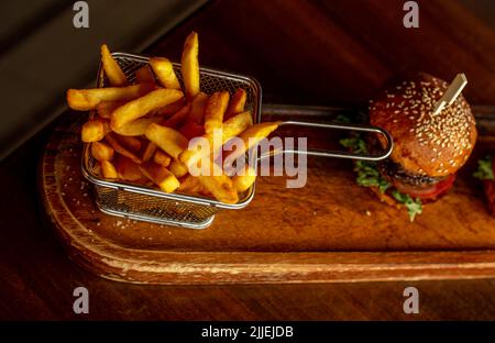 French fries in basket with hamburger on wood. Stock Photo
