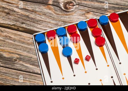 A backgammon board with red and blue checkers and small dices on a wooden table Stock Photo