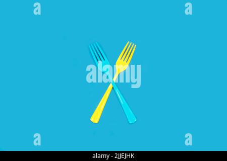 Disposable blue and yellow plastic forks on a blue background with copy space Stock Photo