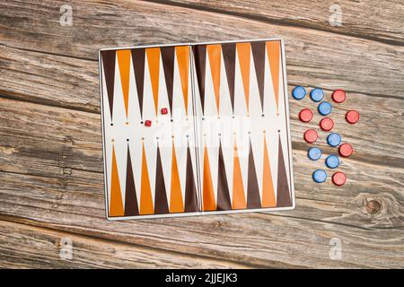 A backgammon board with red and blue checkers and small dices on a wooden table Stock Photo