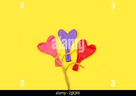 Heart shape deflated colored balloons tied with sisal thread on a yellow background with copy space Stock Photo