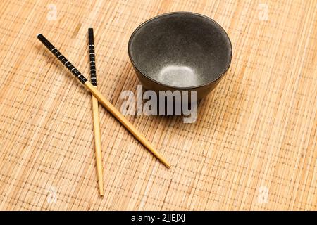 Black bowl and chopsticks on a bamboo table mat in a top view Stock Photo