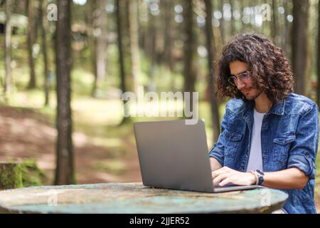 Young latin man sitting in the forest working with laptop freelancing looking laptop focused at Costa Rica. Stock Photo