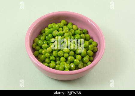 Fresh green peas in pink bowl on light green background Stock Photo